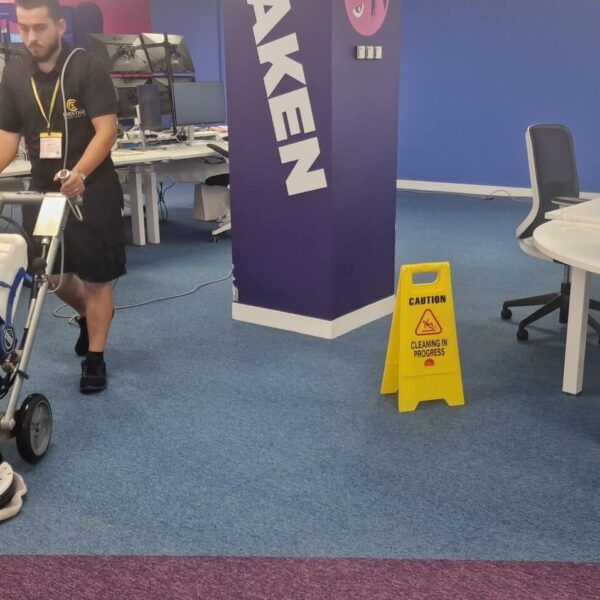 Prestige technician cleaning carpet tiles under desks and around office chairs at Octopus Energy HQ, Oxford Street, using a low-profile Orbot VLM machine.